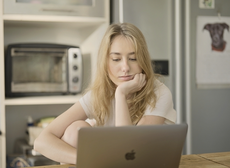 Erschöpfte Frau sitzt nachdenklich vor dem Laptop – Symbol für das Ignorieren eigener Bedürfnisse im Alltag.